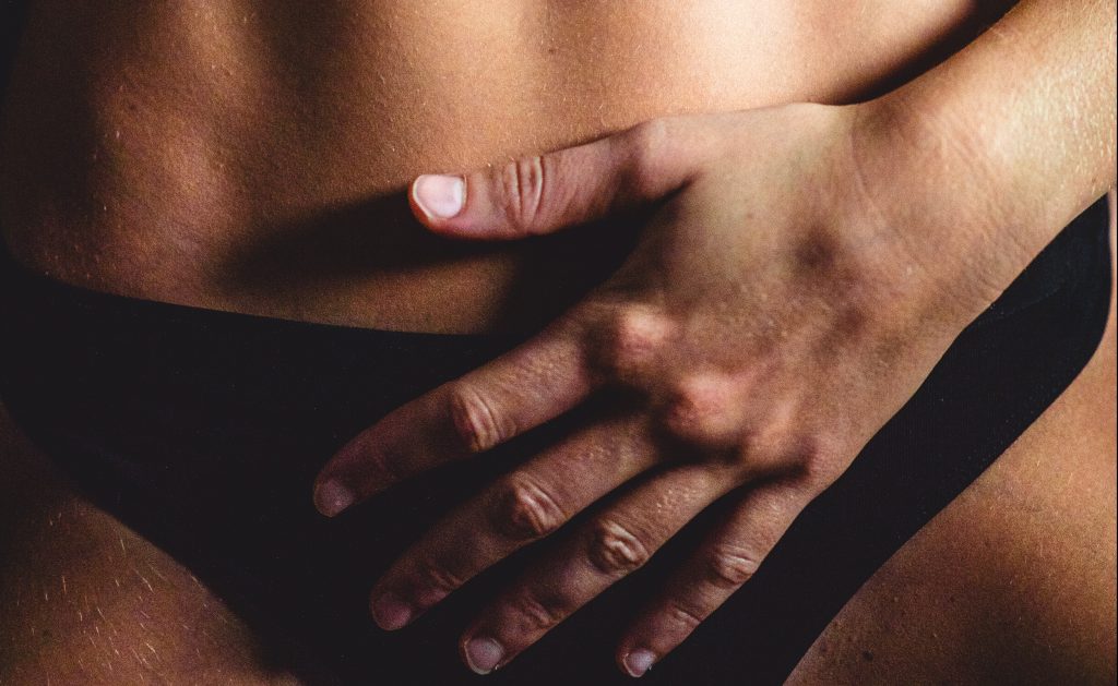 Close-up of a woman's hand placed over her pelvic area, wearing black pants, symbolising pelvic health and awareness.