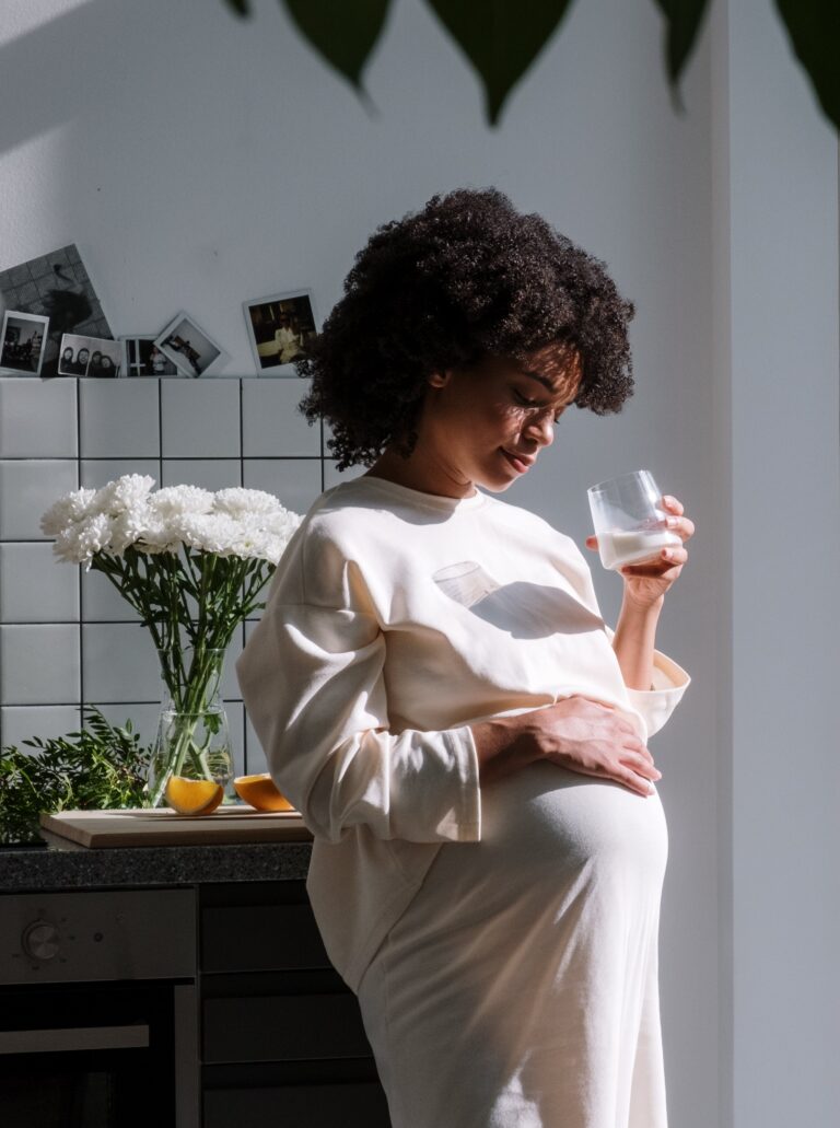 Pregnant woman with a glass in hand drinking and the other hand resting on her pregnant stomach.